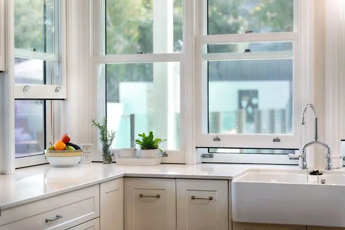 Double hung kitchen windows with operable sashes above white cabinets and farmhouse sink
