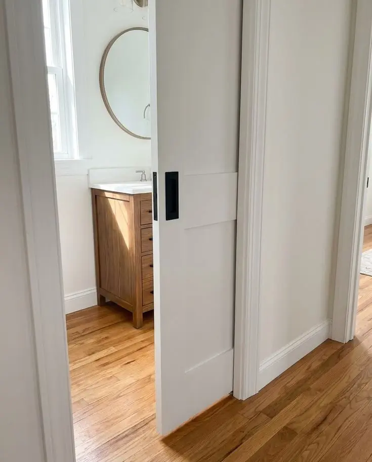 White pocket door with recessed pull opening into a bathroom